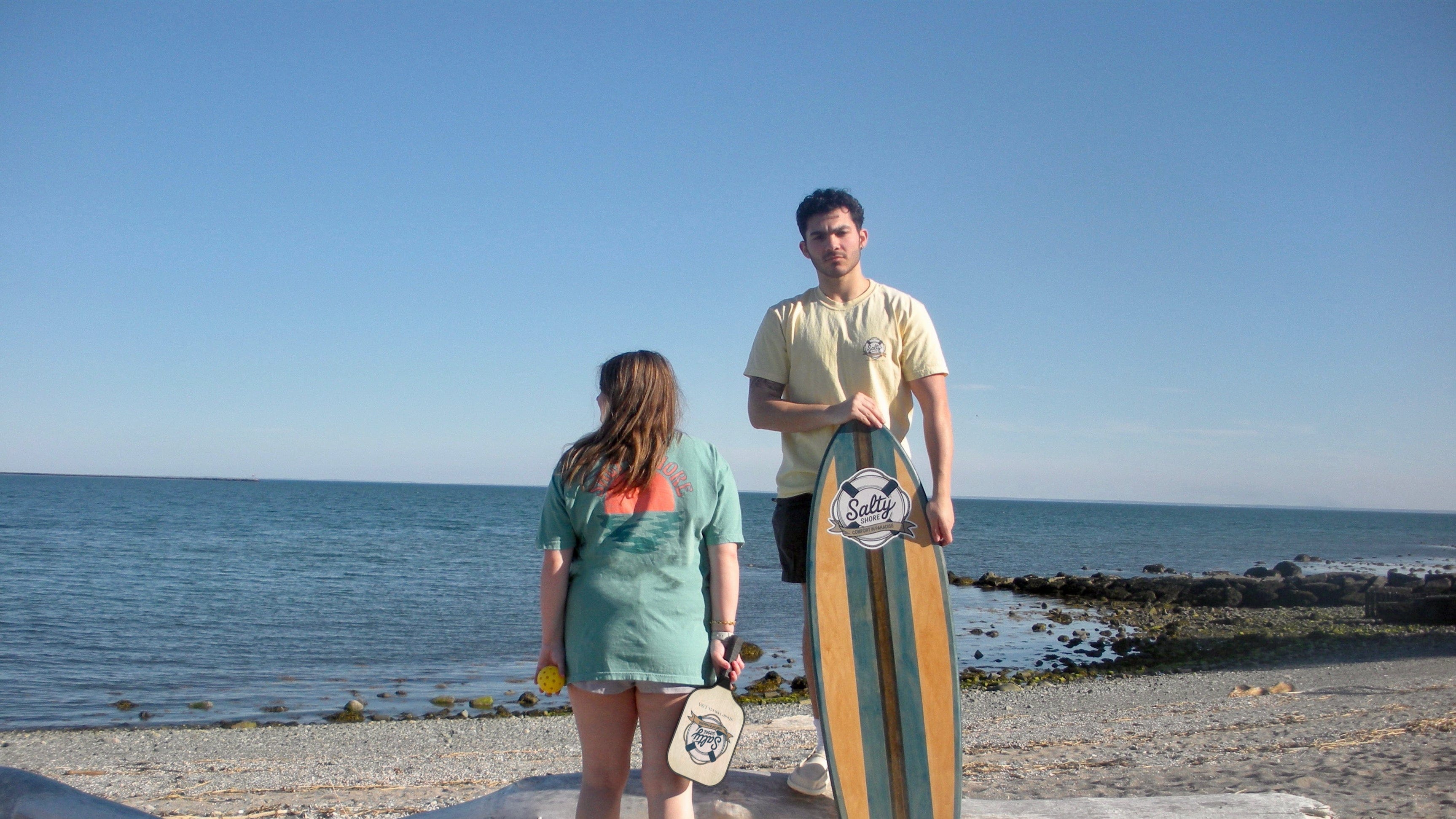 Two people on a beach with one holding a surfboard