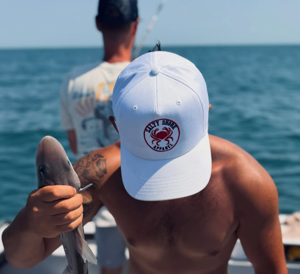 A screenshot of an Instagram post showing a shirtless man on a boat holding a fish, wearing a white baseball cap with a red and black logo. The right side of the screen shows the Instagram interface with the post text and comments.